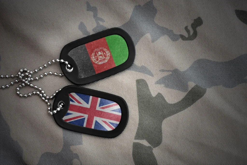 Afghan National Data Breach Explained Featured Image. Image shows two dog tags, one with the United Kingdom flag and the other with the Afghanistan flag on. The dog tags are laid on top of a sand coloured camouflage background.