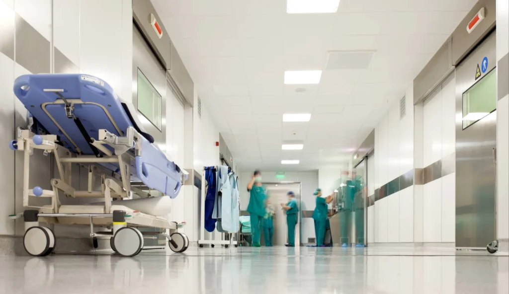 Medical Negligence Claims: What You Need To Know Featured Image. Image shows a hospital corridor with a bed and doctors
