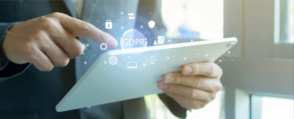 Close up of a mans hand using a tablet with a digital sign overlaying stating GDPR with technology icons